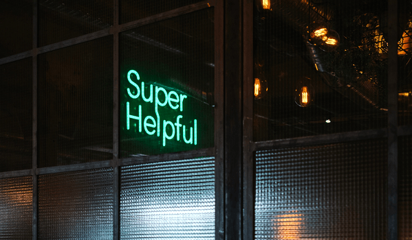 A neon sign cast against a grimy city landscape at night. The sign says Super Helpful.
