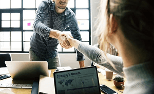 A man leaning over the desk to shake a successful candidates hand. The candidate know what questions to ask in an interview.